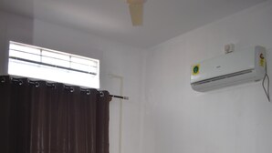 Un dormitorio con una cama de madera, una ventana con cortinas, un equipo de aire acondicionado y un ventilador de techo.