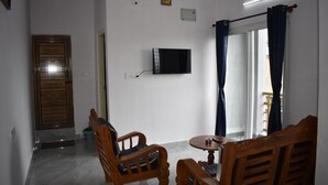 Una habitación con televisor, dos sillas de madera, una mesita, una puerta y una ventana con cortinas.