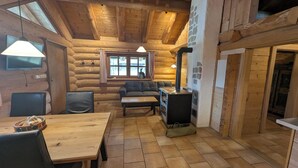 Interior de una cabaña de troncos con una mesa de comedor de madera, un sofá y una chimenea.