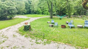 Un espace extérieur verdoyant, avec un chemin de gravier, plusieurs chaises et un hamac.