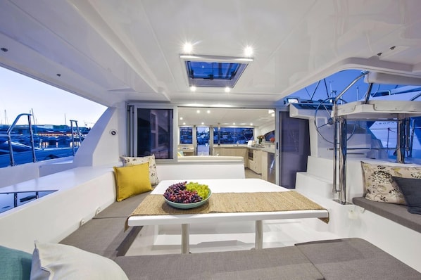 Interior de un yate con comedor, cocina y vista al puerto deportivo.