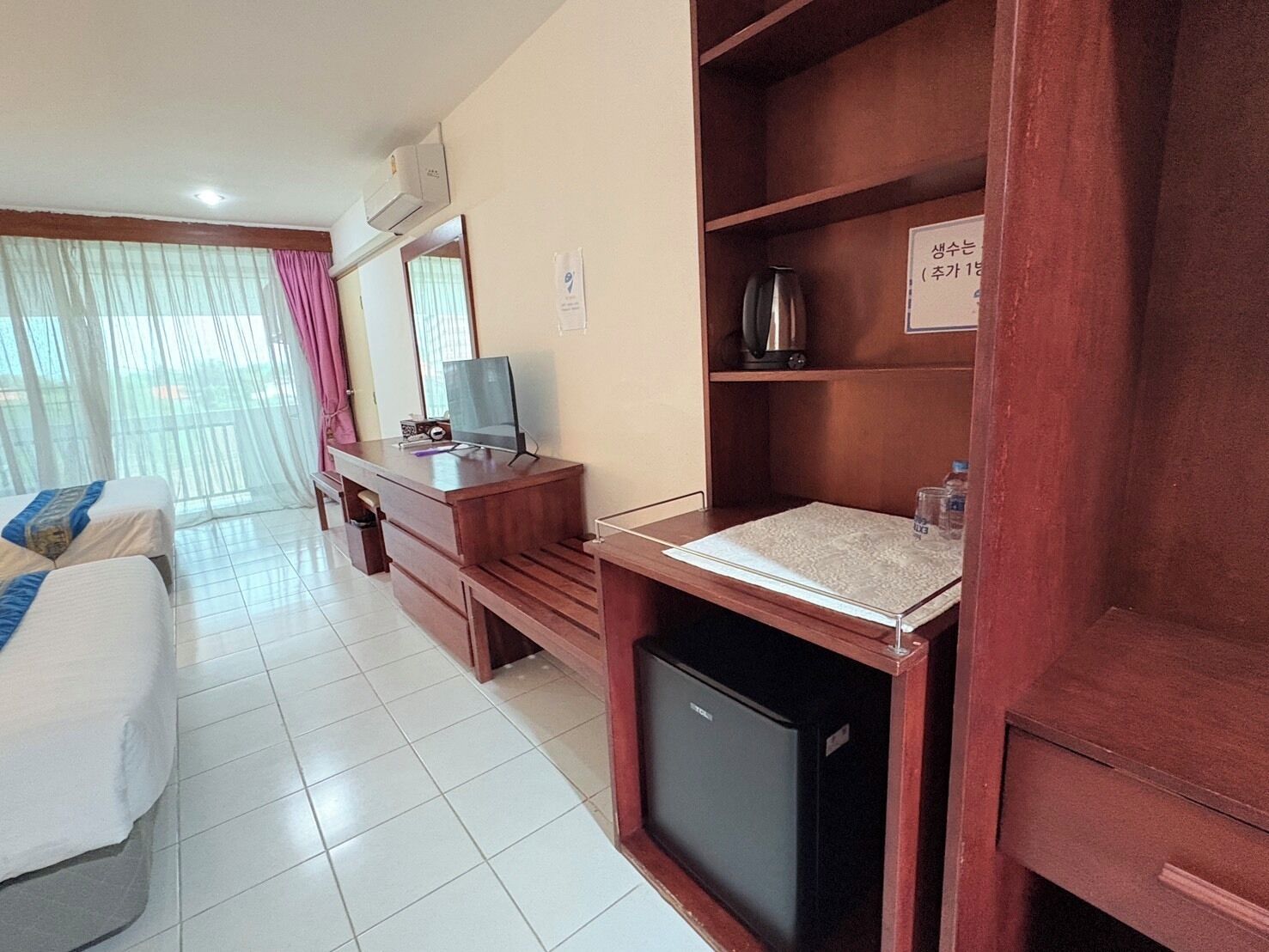 Una habitación de hotel con una cama, un escritorio con computadora, una cafetera y un refrigerador pequeño.