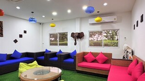 A room with wicker sofas, a glass table, and a ceiling fan. - NJ INTHAI HOTEL (Khlong Luang)