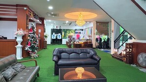 A lobby with a black leather sofa, a wicker coffee table, a Christmas tree, and a reception desk. - NJ INTHAI HOTEL (Khlong Luang)