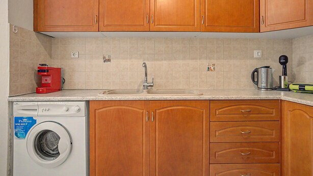 A kitchen with wooden cabinets, a washing machine, a coffee maker, and a kettle. - Apartment 'Dimitra Prive Romantic' with Mountain View, Wi-Fi and Air Conditioning (Zakros)
