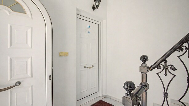 Una puerta blanca con manija, un accesorio de iluminación encima y una escalera de metal con barandilla.