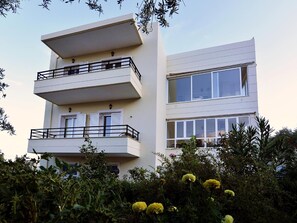 A multi-story building with balconies, large windows, and surrounding vegetation.