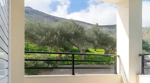 Varanda com vista para campos verdes e oliveiras, corrimão de metal e paisagem montanhosa ao fundo.