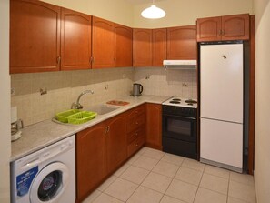 A compact kitchen with wooden cabinets, a washing machine, a stove, and a refrigerator.