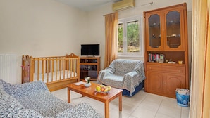 Una sala de estar amoblada con televisión, un aparador de madera con puertas de vidrio, un sofá, una silla y una mesita con fruta.