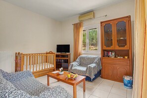 Een gemeubileerde woonkamer met een televisie, een houten kast met glazen deuren, een bank, een stoel en een tafeltje met fruit.