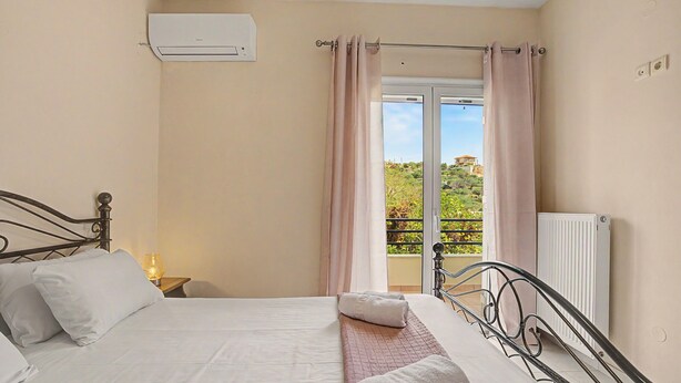 Een slaapkamer met een bed, nachtkastje, airconditioning, raam met gordijnen en een radiator.