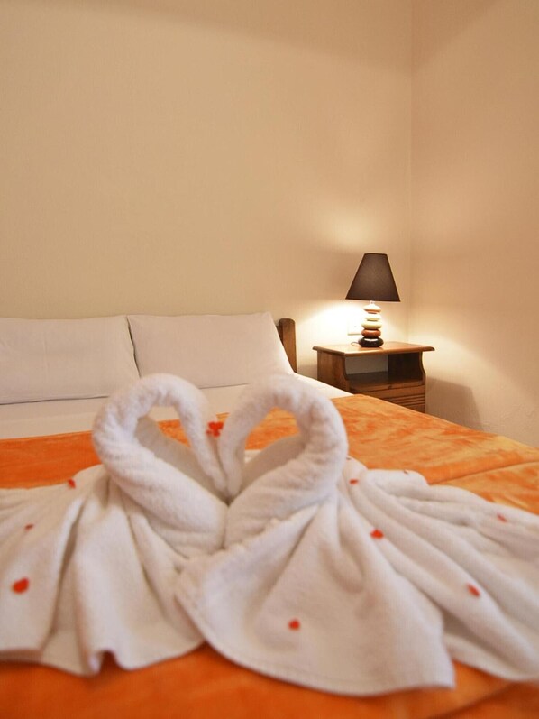 Une chambre d’hôtel avec un lit, une table de chevet sur laquelle se trouve une lampe, et une serviette disposée avec soin sur le lit.