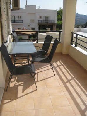 Un balcon avec une table et des chaises, une vue sur les immeubles et un sol carrelé.