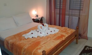 Uma cama com um edredom branco e laranja, um painel de cabeceira de madeira e uma mesa de cabeceira com uma luminária.