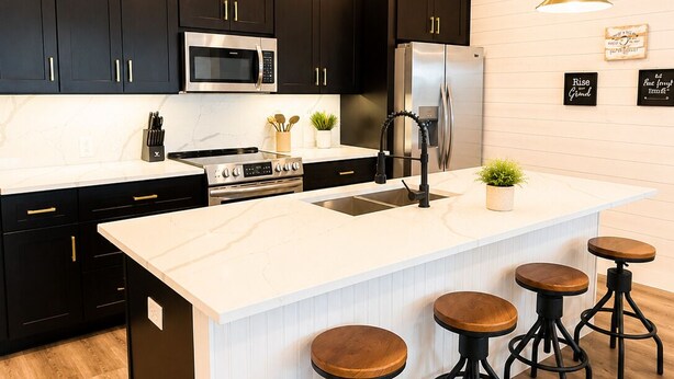 A modern kitchen with dark cabinets, stainless steel appliances, a large island with stools, pendant lighting, and a white backsplash. - 3 BD Family Home | Extd Stays | Pets Ok (Aransas Pass)