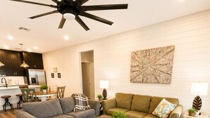 A modern living room with a ceiling fan, two sofas, a coffee table, and a kitchen in the background. - 3 BD Family Home | Extd Stays | Pets Ok (Aransas Pass)