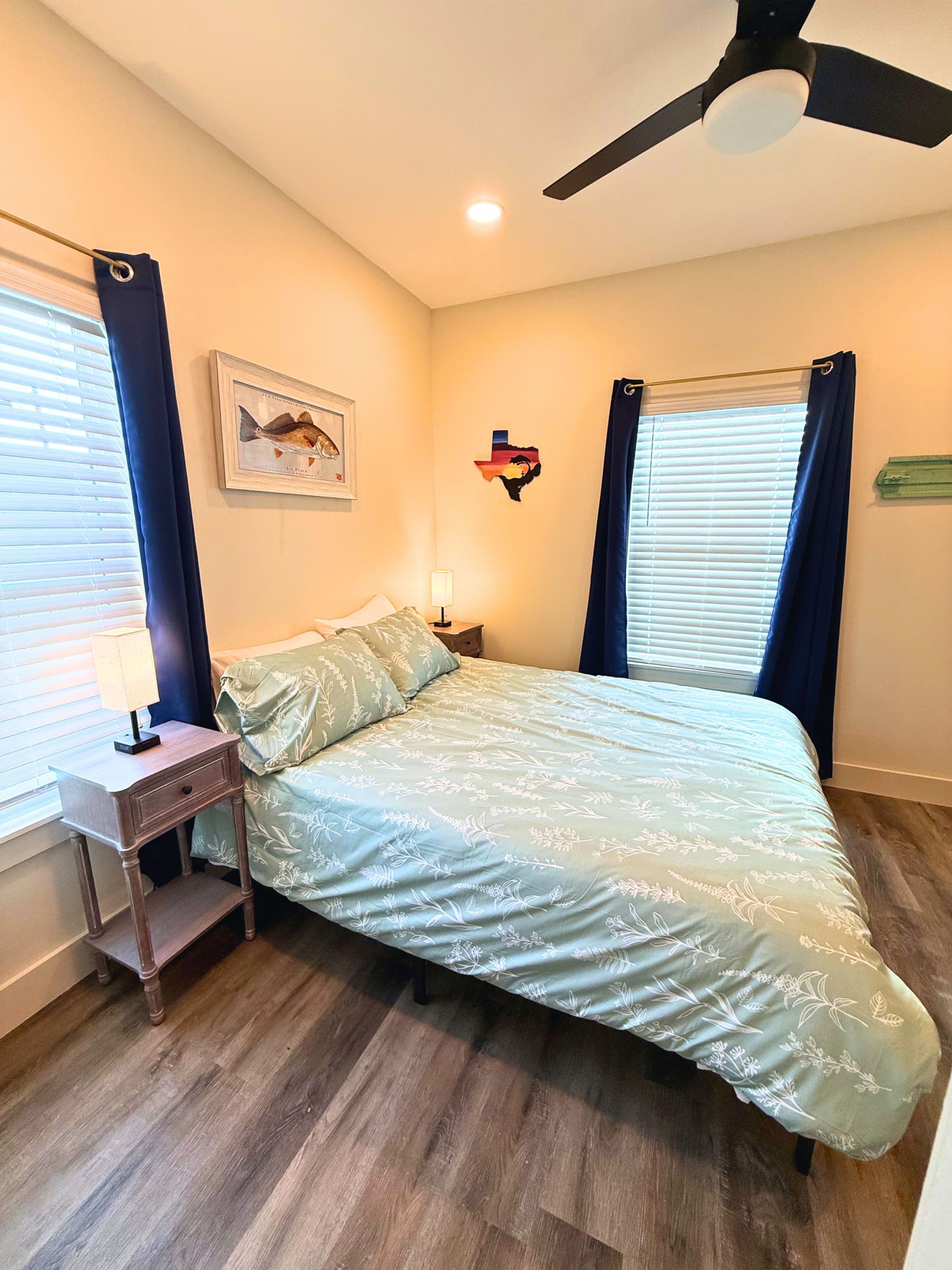 Une chambre à coucher comprenant un lit, une table de chevet, un ventilateur de plafond et une étagère fixée au mur.
