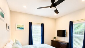 A bedroom with a bed, a ceiling fan, a TV, a dresser, a bedside table with a lamp, and a window with curtains. - 3 BD Family Home | Extd Stays | Pets Ok (Aransas Pass)