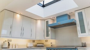 Eine moderne Küche mit Oberlichter, weißen Schränken und einer blauen Dunstabzugshaube.