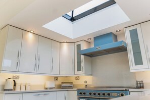 A modern kitchen with a skylight, white cabinets, and a blue range hood.