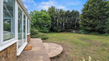 A house with a stone pathway leading to a grassy yard, surrounded by trees.