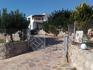 Uma entrada com portão para um edifício, com um caminho de pedras que leva a ele, cercado por árvores e uma cerca de metal.