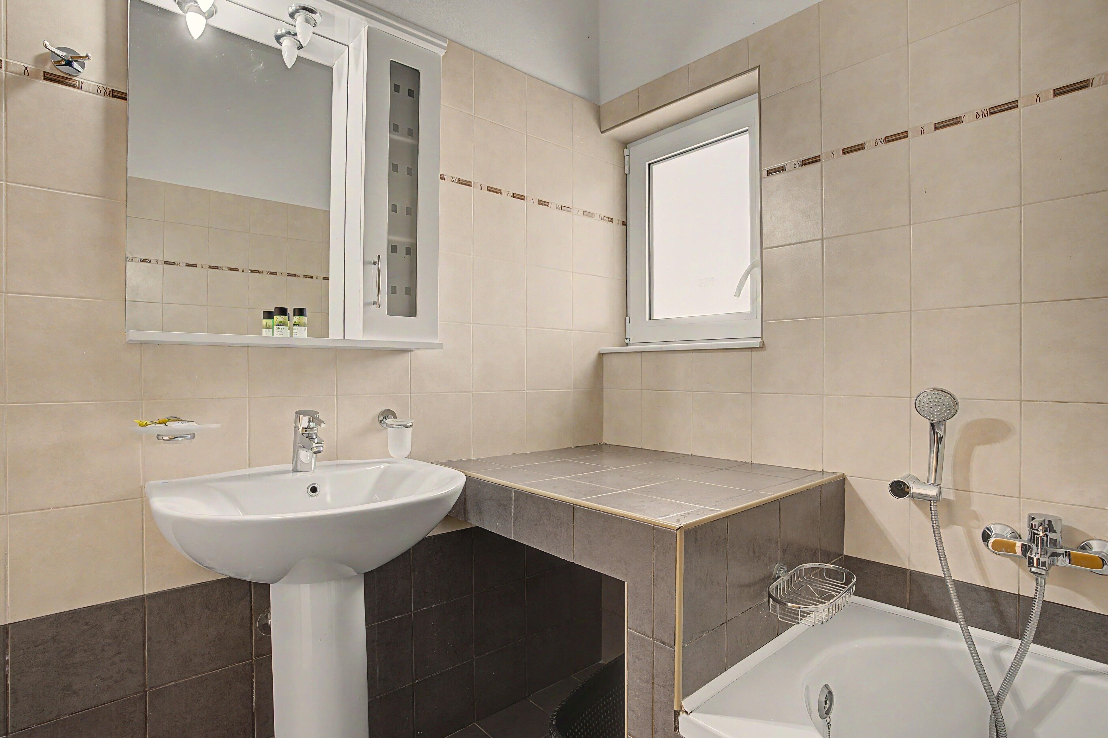 A bathroom with a white sink, a mirror, a window, and a shower.