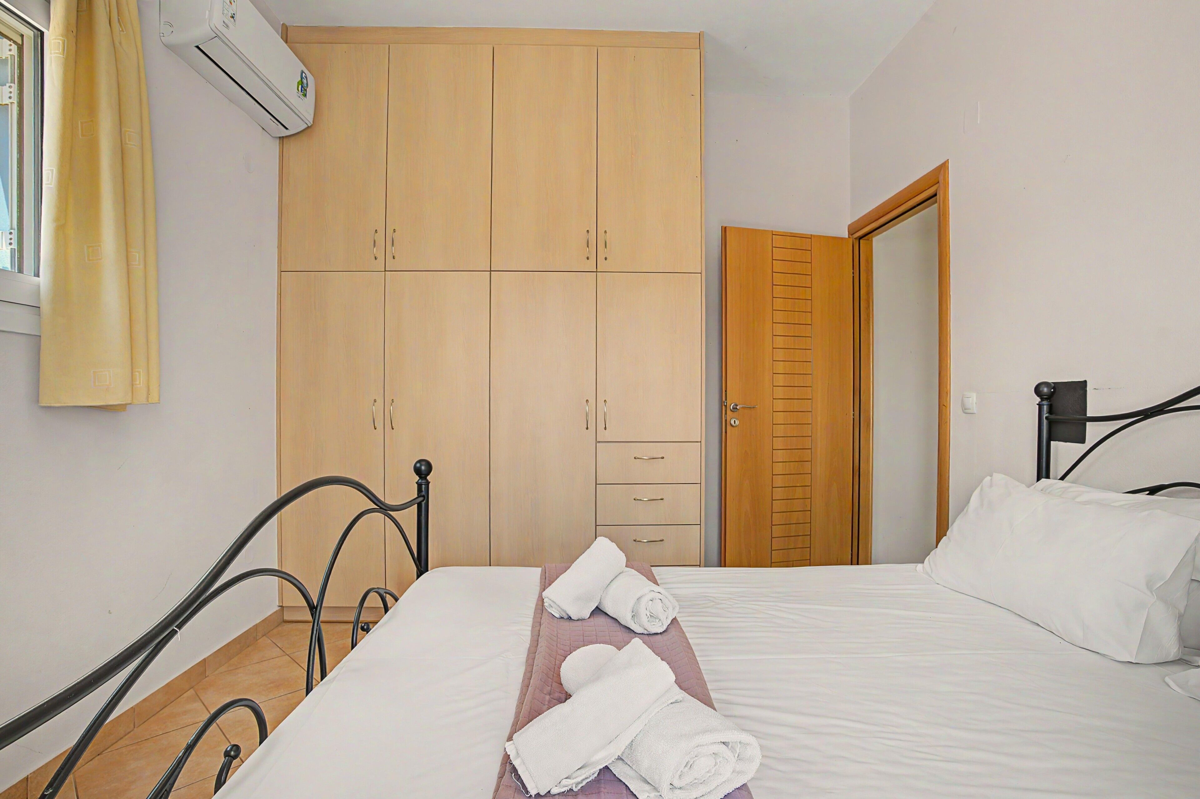 Une chambre à coucher avec un lit, une armoire en bois, une porte de salle de bain et une fenêtre avec des rideaux.