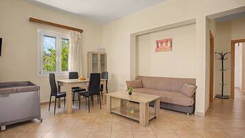 A living room with a sofa, a dining table with chairs, a cabinet, and a window with curtains.