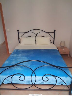 Un lit avec une couvre-lit aux motifs de ciel bleu, une tête de lit en métal noir et une table de chevet avec une lampe.