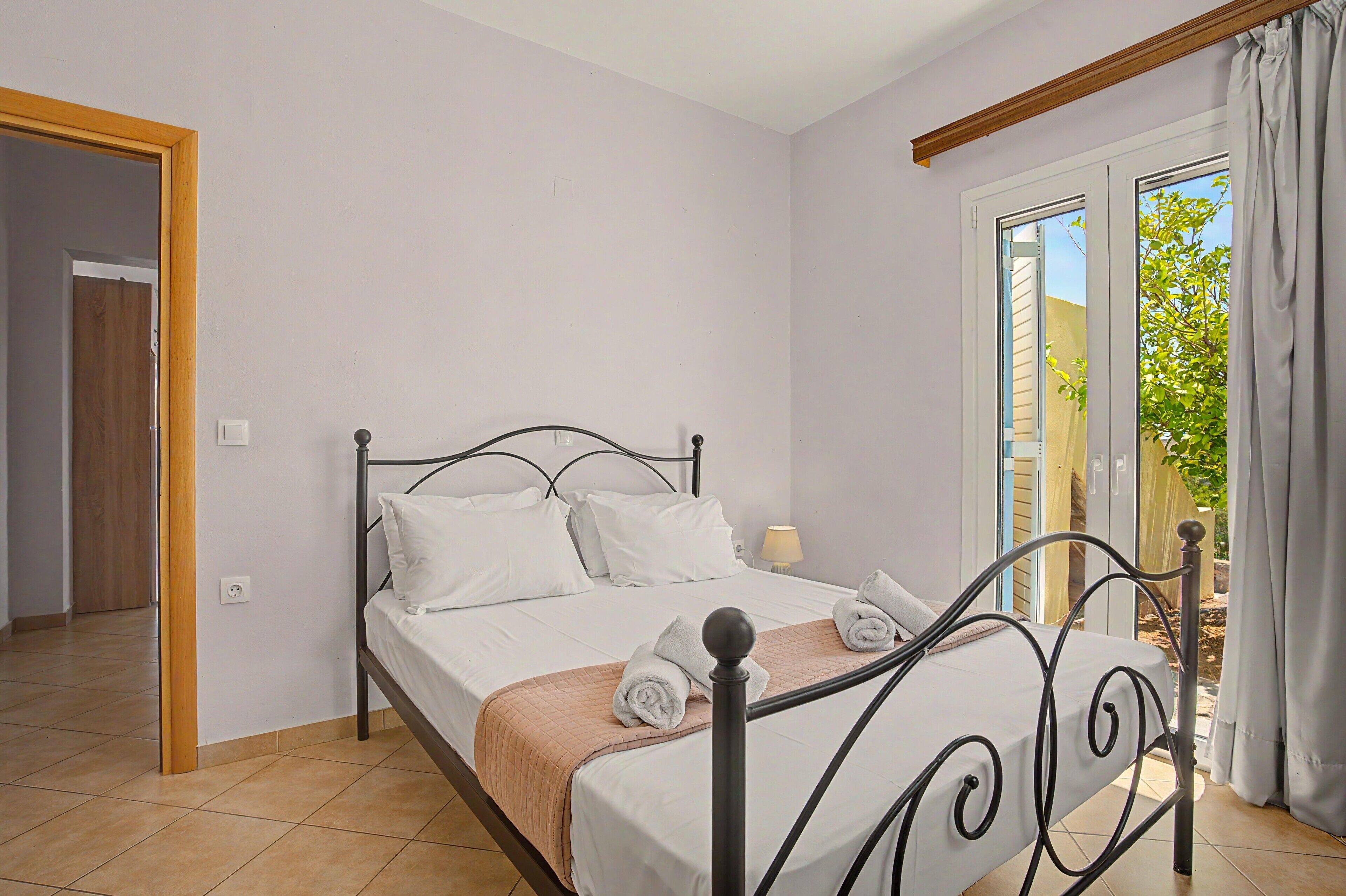 A bedroom with a bed, a window with curtains, a door, and a tiled floor.