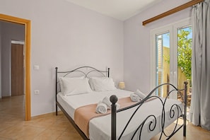 Ein Schlafzimmer mit einem Bett, einem Fenster mit Vorhängen, einer Tür und einem gefliesten Boden.