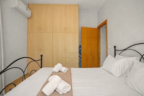 Une chambre à coucher comprenant un lit, une armoire en bois, une table de chevet avec des serviettes et une porte donnant sur une autre pièce.