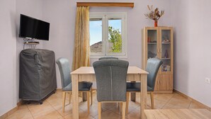 Een kamer met een eettafel, stoelen, een televisie, een kast en een raam met gordijnen.