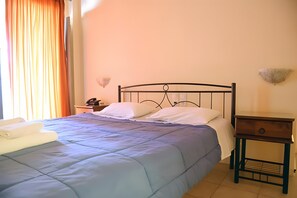 Uma cama com cabeceira, mesa de cabeceira com gaveta e luminária fixada na parede.