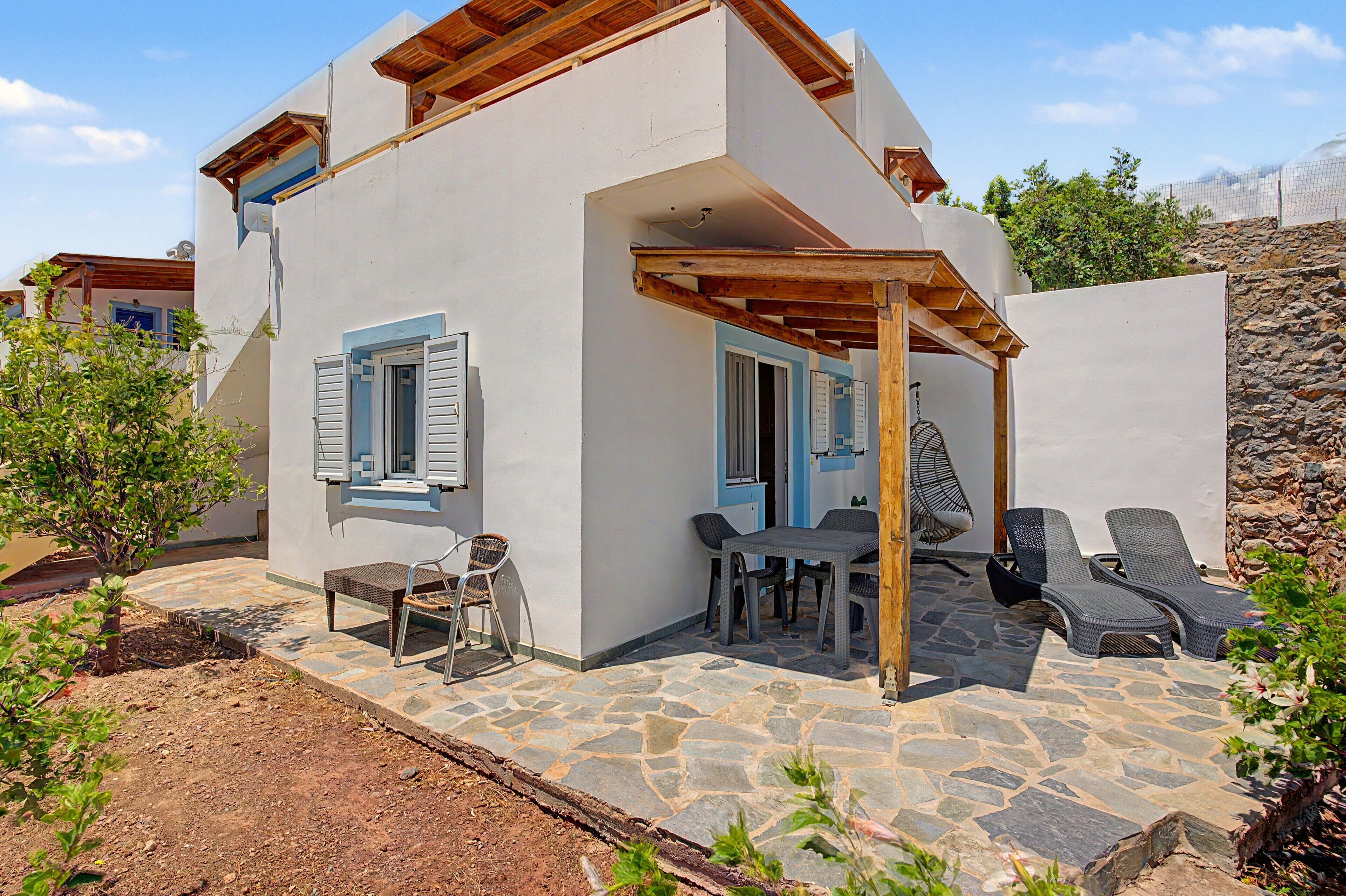A two-story house with a stone patio, outdoor seating, and a wooden pergola.