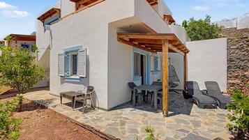 A two-story house with a stone patio, outdoor seating, and a wooden pergola.