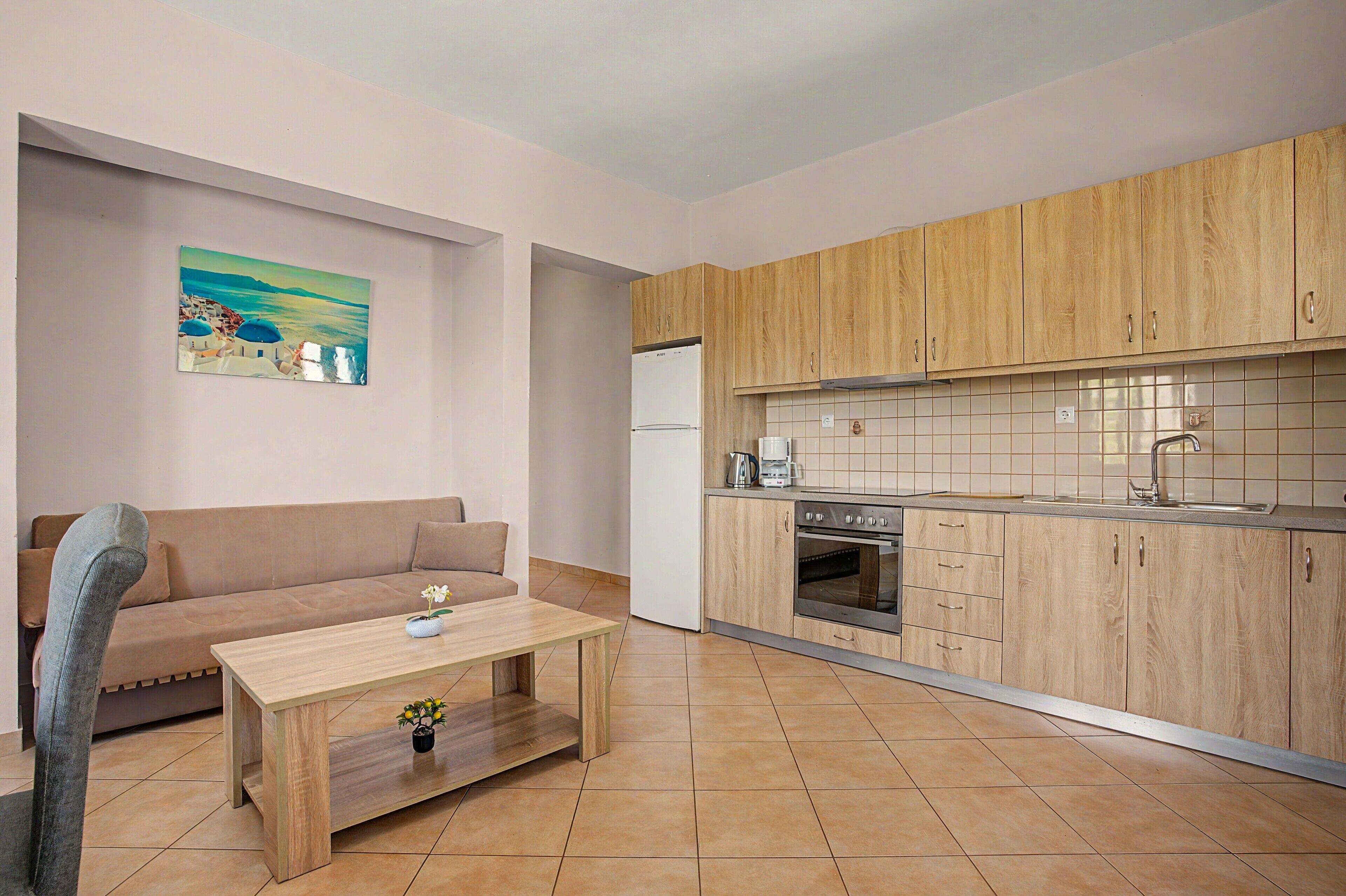 A compact living space with a kitchenette, a sofa, a coffee table, and a painting on the wall.