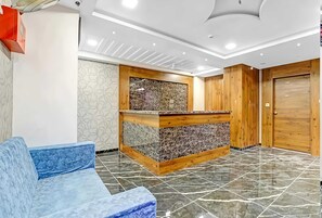 A reception area with a marble counter, a blue sofa, and a wooden door. - Classic Hotel Navjivan (Ahmedabad)