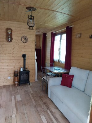 Interior acogedor de una cabaña con techo de madera, una mesa de comedor, un sofá, una estufa y un reloj en la pared.