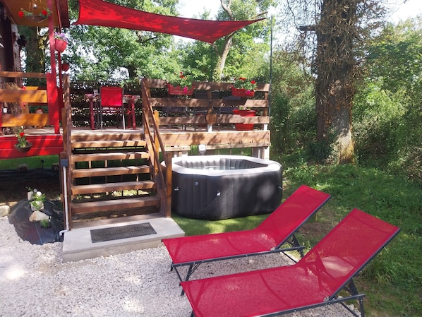 Una terraza de madera con jacuzzi, sillas rojas y una valla de madera decorada con macetas colgantes.
