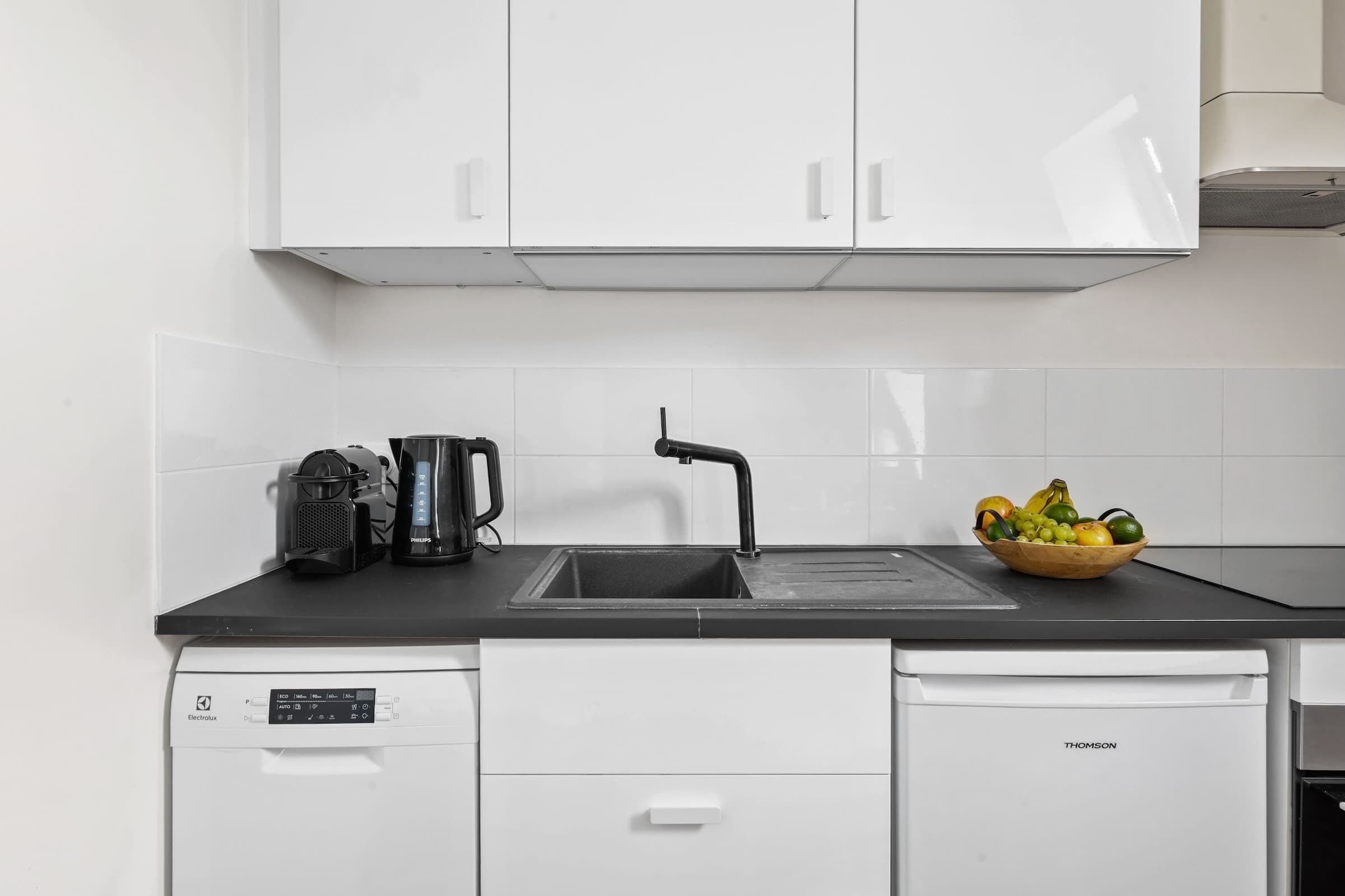 A kitchen with a black countertop, white cabinets, a dishwasher, and a fruit bowl.