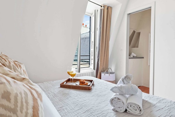 A hotel room with a bed, a tray with breakfast, a towel, and a view of the outside. - Stylish 1BR in the Marais - Rue des Archives (Paris)