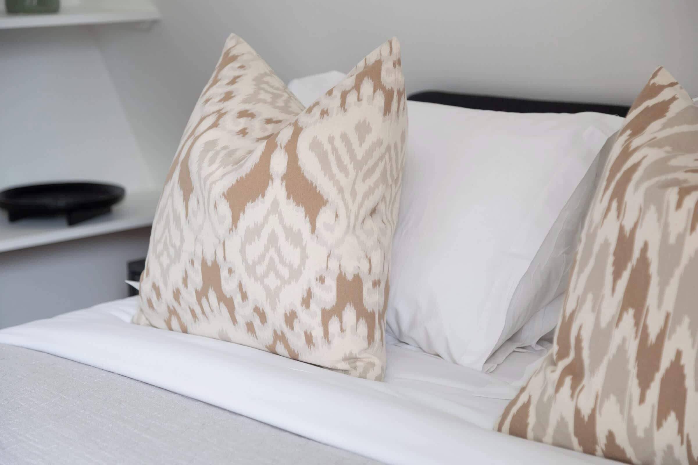 A bed with white bedding and patterned pillows.