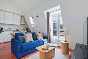 A modern living room with a blue sofa, a wooden coffee table, and a view of buildings through a window. - Stylish 1BR in the Marais - Rue des Archives (Paris)