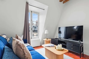 A modern living room with a sofa, TV, and a small side table. - Stylish 1BR in the Marais - Rue des Archives (Paris)