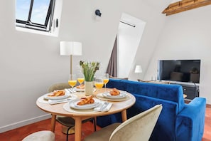 A dining area with a round table, blue sofa, and a TV. - Stylish 1BR in the Marais - Rue des Archives (Paris)