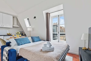 A hotel room with a bed, a desk with breakfast, a window with a view, and a balcony. - Stylish 1BR in the Marais - Rue des Archives (Paris)