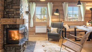 A cozy room with a stone fireplace, a comfortable sofa, a dining table, and a view through large windows. - Holiday Home With a Terrace and Mountain Views (Koscielisko)